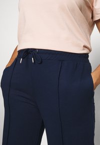 Pantaloni sportivi blu navy con vita regolabile, tasche laterali e sottili cuciture verticali. Realizzati in un morbido tessuto testurizzato per il massimo comfort.