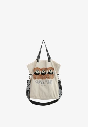 Bolsa tote beige con tres ositos de peluche marrones que llevan camisetas negras y una correa de hombro y asas de marca en blanco y negro.
