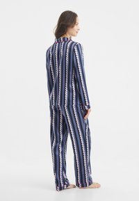 Marineblauwe gestreepte pyjama set gemaakt van zachte stof. Heeft zigzagpatronen in roze en wit, met contrasterende accenten op de manchetten en de kraag.
