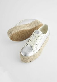 Baskets blanches avec un embout métallisé argenté, tige en textile et semelle en jute tissé. Comprend des lacets et une semelle extérieure en caoutchouc texturée.