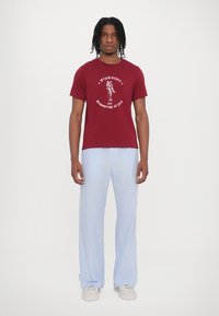 Maroon cotton t-shirt with a white graphic print, paired with light blue and white striped wide-leg pants, worn with white sneakers.
