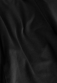 Čierny textil s hladkou štruktúrou, ukazujúci jemné vlny a záhyby, ktoré zvýrazňujú jeho mäkkú a ľahkú povahu.