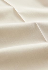 Tissu beige clair et doux avec une texture lisse, présentant des motifs tissés subtils et de délicates ondulations. Idéal pour diverses applications textiles.