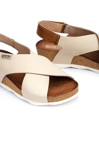 Beżowe skórzane sandały zakryte z przodem z paskiem krzyżowym i brązowym zapięciem na kostkę. Wkładka korkowa z teksturowaną brązową wkładką.