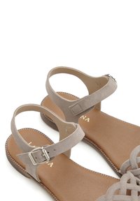 Gray suede sandals with ankle straps, open toe design, and brown faux leather insoles. Features a metal buckle and woven upper style.