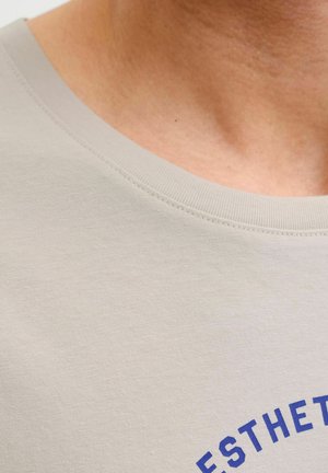 Gros plan sur le cou et le haut de la poitrine d'une personne portant un t-shirt beige clair avec un texte bleu partiellement visible.