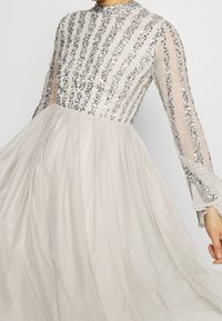 Robe à manches longues en gris clair avec un corsage à sequins ajusté et une jupe en tulle fluide, ornée de détails en perles délicates et de manches transparentes.