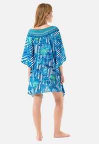 Kaftán con un patrón de hojas tropicales en azul y verde, con acentos a rayas y un escote bordado texturizado. Corte holgado, hasta la rodilla.