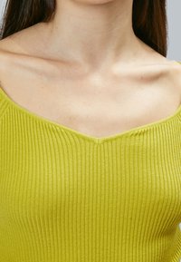 Rippenshirt mit V-Ausschnitt in leuchtendem Limettengrün. Aus weichem Stoff gefertigt, mit einer figurbetonten Passform und subtiler Textur, die eine klare und schlichte Silhouette zur Schau stellt.