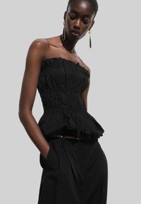 Svart strapless topp med rynkad textur och volangkant. I kombination med hög midja svarta byxor, som har en kedjedetalj i midjan.