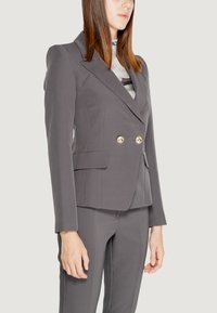 Blazer grigio doppiopetto con bottoni dorati, dotato di una vestibilità su misura, revers a punta e tessuto liscio. Abbinato a pantaloni coordinati.