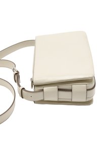 Beżowa skórzana torba crossbody o kwadratowym kształcie, z regulowanym paskiem, zamknięciem na zamek oraz poziomym panelem wykończeniowym po boku.