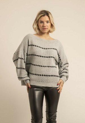 Pull en maille gris avec des motifs d'étoiles noires, coupe oversized, encolure large et poignets côtelés. Associé à un pantalon en cuir noir.
