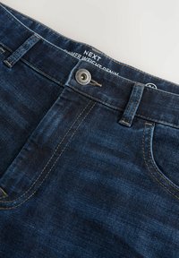 Jeans de mezclilla azul oscuro con corte recto, cuentan con un cierre de botón, trabillas para el cinturón y una textura de desgastado sutil. Logo en la cinturilla.