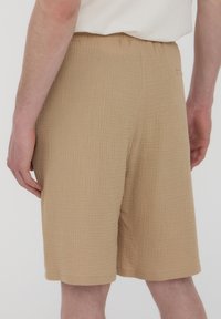 Bermuda kaki con un tessuto testurizzato, vestibilità dritta, tasche laterali e una vita elasticizzata. L'orlo arriva appena sopra il ginocchio.