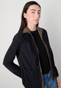Schwarze Jacke mit Leopardenmusterkragen. Verfügt über eine Vordertasche und ein tailliertes Design. Das Material wirkt glatt und hat eine lockere Passform.