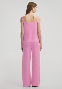 Rosa gestrickter Tanktop und weite Hose, beide mit einem strukturierten Muster. Der Stoff hat ein weiches Aussehen mit einer lässigen Silhouette.