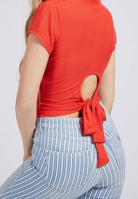 Rød kortærmet top med udskæring i ryggen og bånddetalje, parret med blå og hvide stribede højttaljede jeans med baglommer.