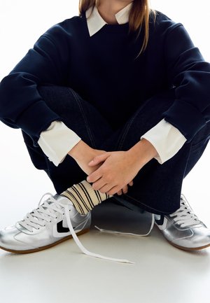 Marinblå oversized sweatshirt med vit krage, mörka jeans, silverfärgade sneakers och randiga krämfärgade strumpor. Sneakers har vita snören och svarta detaljer.