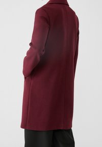 Bordeauxfarbener Wollmantel mit langen Ärmeln und strukturiertem Schnitt. Verfügt über einen Reverskragen, Seitentaschen und eine glatte, weiche Textur.