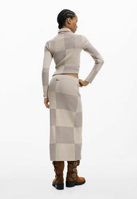 Conjunto beige de dos piezas tejido con canalé vertical, cuello alto y falda larga. Botas marrones de ante con hebillas complementan el conjunto.