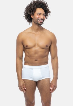 Boxer shorts bianchi in cotone con una texture a costine e un elastico in vita, indossati da un uomo con capelli ricci, in piedi contro uno sfondo neutro.