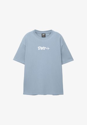 Svetlo modra bombažna majica s sproščenim krojem, ki ima belo vezeno besedilo "STWO" in podrobnost letala. Kratkimi rokavi, okrogel izrez.