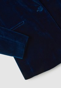 Blazer de terciopelo azul marino con solapa elegante, cierre de un solo botón y hombros estructurados, que presenta una textura suave y un corte a medida.