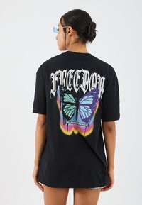 Black oversized t-shirt featuring a colorful butterfly graphic, "FREEDOM" text, and a bold design with gradient accents. Short sleeves.