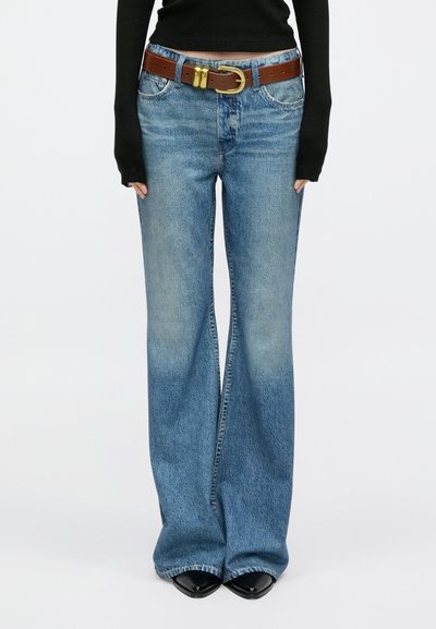 Jeans de ganga azul claro com corte flare e cintura média, apresentam um cinto de couro castanho com fivela dourada e costuras contrastantes.