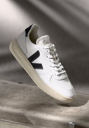 Baskets en cuir blanc avec un embout texturé, accents bleu marine foncé et détails perforés. Comprend une semelle en caoutchouc crème et un design à lacets.
