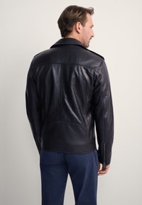 Czarna skórzana kurtka motocyklowa o dopasowanym kroju, z dużym kołnierzem i zapinanymi na zamek mankietami. Posiada przeszycia dekoracyjne i gładką fakturę.