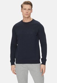 Felpa blu navy in misto cotone, con collo e polsini a costine, e logo 'GUESS' in rilievo sulla parte anteriore.