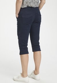 Mörkblå korta cargo-byxor med flera fickor, texturerad tyg och en något avsmalnande benform, matchat med vita skor.