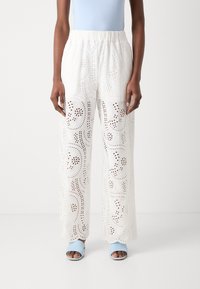 Pantaloni bianchi, leggeri e a gamba larga con dettagli a motivo tagliato al laser. Vita elasticizzata abbinata a sandali blu a scivolo.