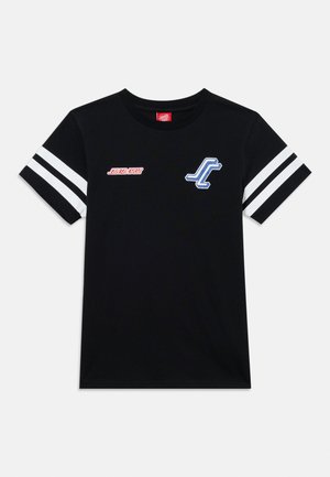 Juoda trumpomis rankovėmis marškinėliai su baltais dviem dryžiais ant rankovių, raudonu užrašu „Santa Cruz“ kairėje krūtinės pusėje ir mėlynu bei baltu „SC“ logotipu dešinėje krūtinės pusėje.