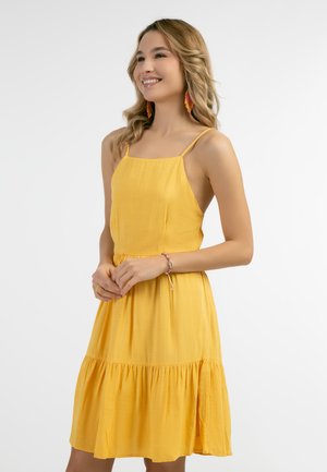 Gelbes ärmelloses Kleid mit gerafftem Taillenschnitt und gestuftem, schwingendem Saum. Glattes, leichtes Material mit einem dezenten Glanz. Keine Muster oder Akzente.