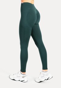 Leggings verdi a vita alta in tessuto elastico, caratterizzati da un design sagomato e una texture liscia, abbinati a scarpe da ginnastica bianche.