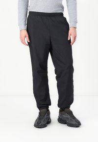 Pantaloni jogger negri cu talie elastică, design ușor, picioare conice și mansete elastice, asociați cu teneși negri texturați.