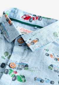 Hellblaues Hemd mit Fischgrätmuster, das bunte gestickte Rennwagen zeigt. Mit Button-Down-Kragen und braunen Knopfdetails.