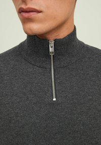 Maglione in maglia grigio scuro con colletto alto e zip frontale. Il tessuto è liscio con una texture sottile e dettagli a coste sul colletto.