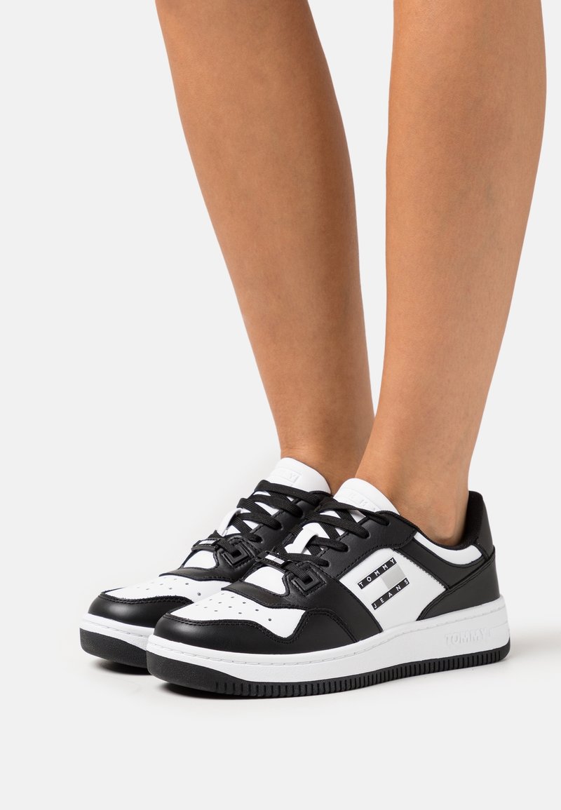 Baskets en cuir noir et blanc avec un bout arrondi, des perforations décoratives, des lacets noirs et des accents de logo sur les côtés.