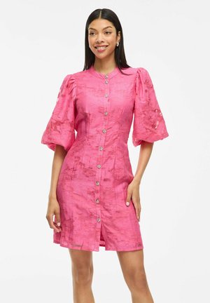 Kort rosa klänning med puffärmar, texturerad tyg, framknäppning och runda knappar. Kjolens längd når mitt på låret.