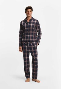 Marinblå rutigt pyjamaset med en skjorta med knappar och byxor med raka ben. Har röda och vita rutnätslinjer, tillverkad av mjukt tyg.