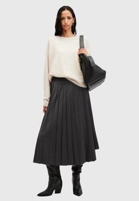Lichtbeige fuzzy trui, donkergrijze plissé maxi rok en zwart leren laarzen tot de knie. Zwarte handtas met een gestructureerd ontwerp.