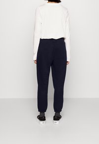 Marina blå sweatshirtbyxor med elastiska mudd och midja, i kombination med en vit långärmad skjorta och svarta platåskor med grå strumpor.