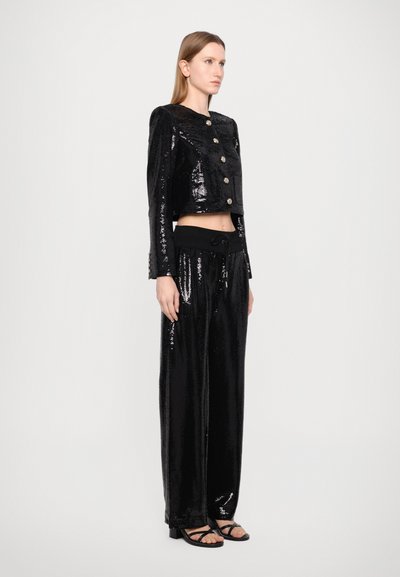 Black sequined cropped jacket with button closures, paired with matching loose pants featuring a black elastic waistband and sandals.