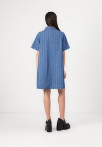 Denim kleita ar īsām piedurknēm, vertikālām baltām svītrām, apkakli un neapstrādātu apakšmalu. Kombinēta ar melnām platformām.