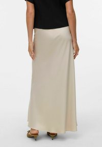 Gonna maxi di un beige chiaro, tessuto morbido, design fluido, lunghezza alla caviglia. Abbinata a un top nero e tacchi beige.