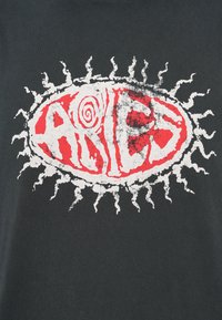 Tricou negru cu un grafic circular proeminent cu un design roșu și alb, spirale și raze solare ascuțite. Textul spune „ARIES”.